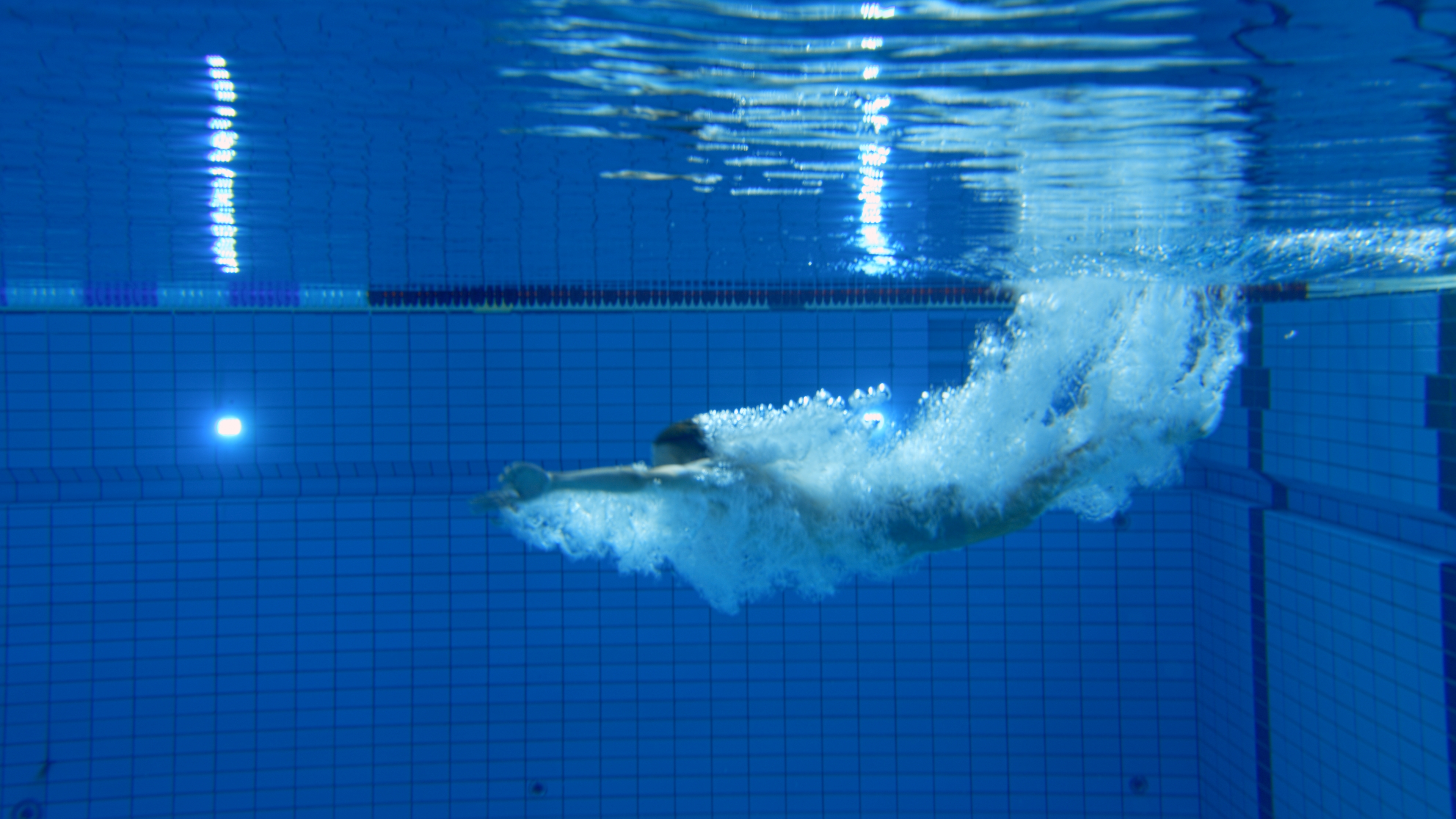 Ein Schwimmer im Wasser eines Schwimmbeckens, der sich in einer sportlichen Pose befindet. 