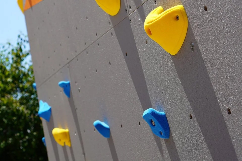 Kletterwand mit farbigen Griffen. Kletterwand mit blauen und gelben Griffen, die zum Klettern einladen, vor einem neutralen Hintergrund.