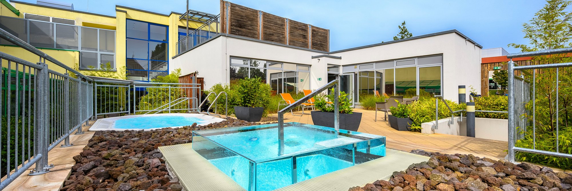 Zeitgenössisches Haus mit einem Pool und dekorativen Felsen, umgeben von Pflanzen und einem blauen Himmel.