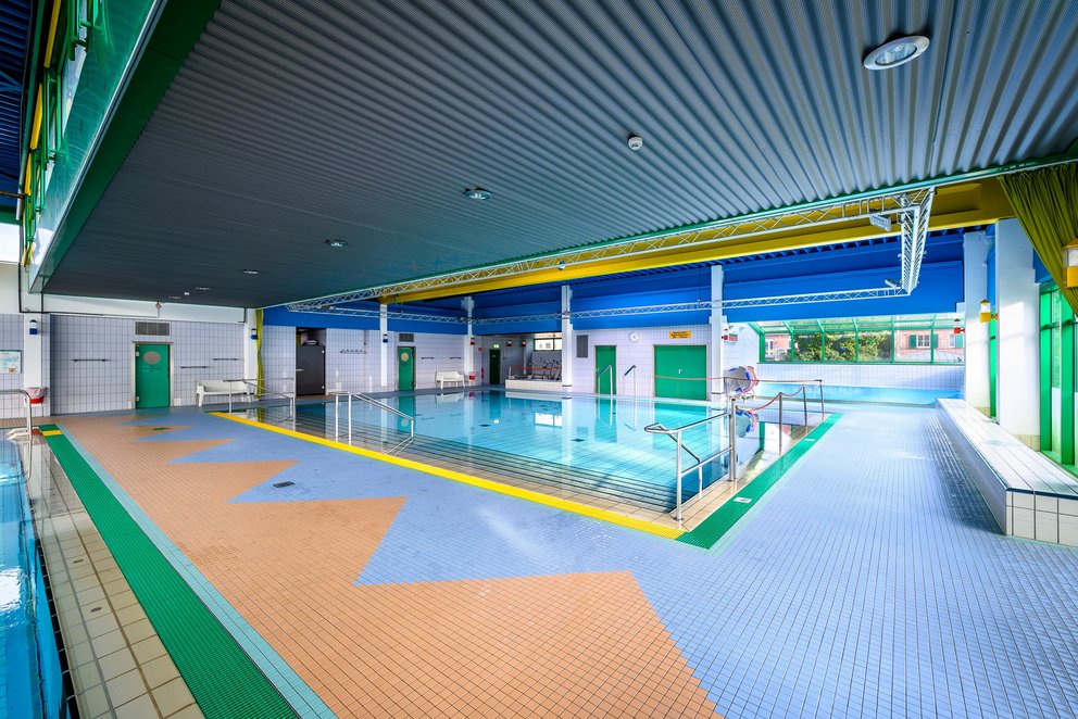 Lehrschwimmbecken in heller Hallenatmosphäre. Großes Lehrschwimmbecken mit blauem Deckenanstrich in einem Innenraum.