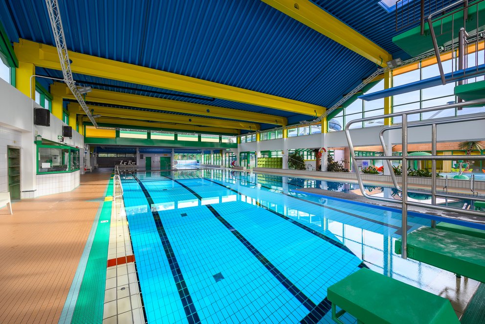Ein Hallenbad im sanften Licht. Weitläufiges Hallenbad unter einer blauen Decke, das Licht reflektiert sich sanft auf der Wasseroberfläche.