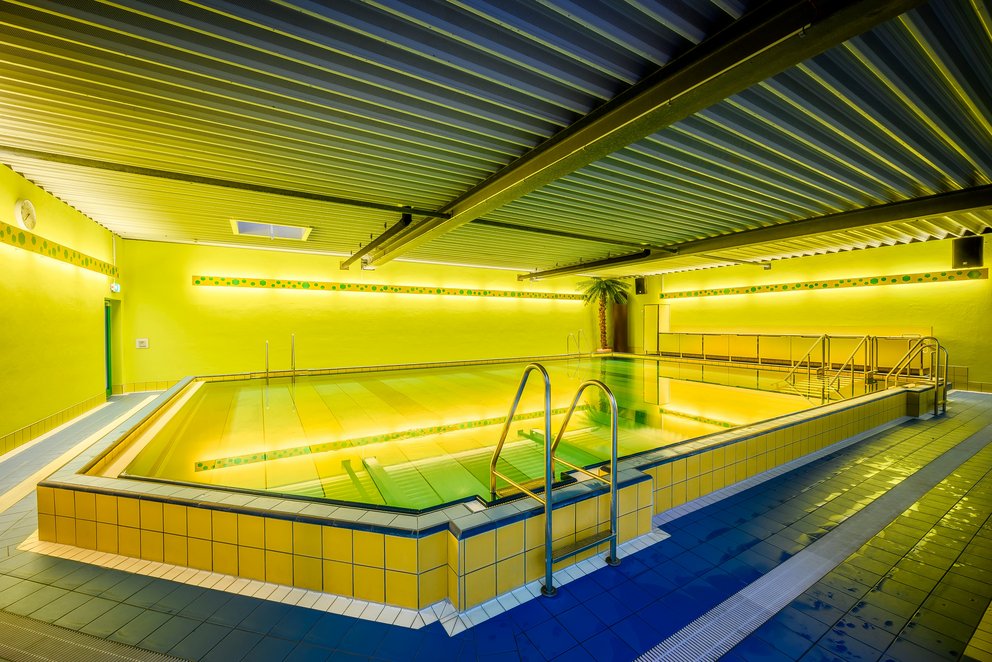 Vom Workout zur Wochenendpause – Dein Hallenbad für jede Stimmung Weitläufiges Hallenbad mit gelben Wänden, geeignet für Fitnesskurse, ruhig an Werktagen, lebhaft an Wochenenden