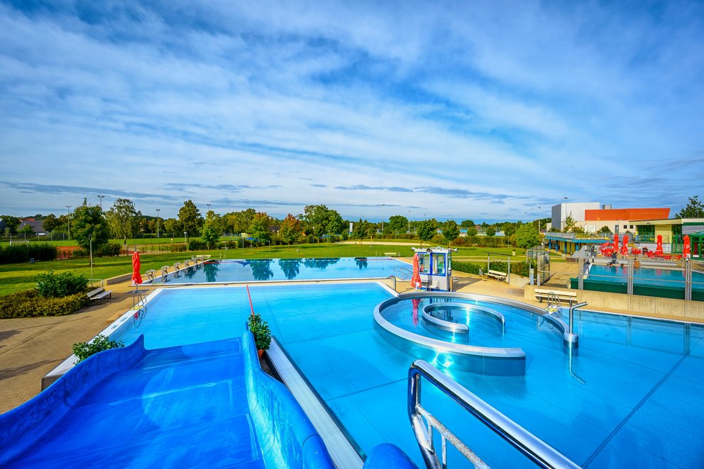 Weitläufiger Pool-aussen Weitläufiger Pool mit einer bunten Rutsche, die ins Wasser führt, umgeben von Erholungsbereichen.