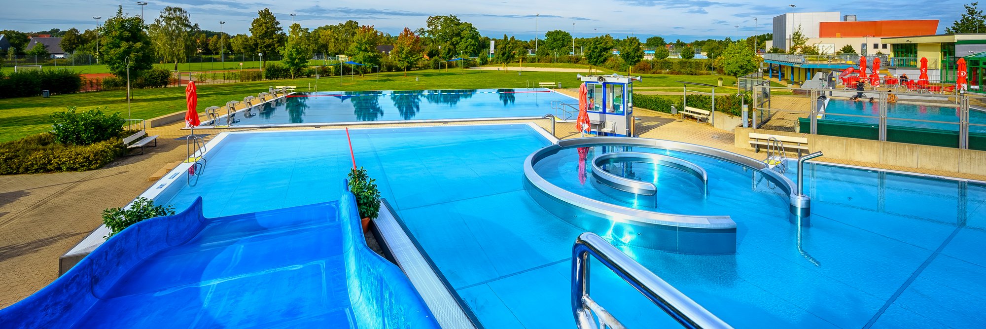 Weitläufiger Pool-aussen Weitläufiger Pool mit einer bunten Rutsche, die ins Wasser führt, umgeben von Erholungsbereichen.