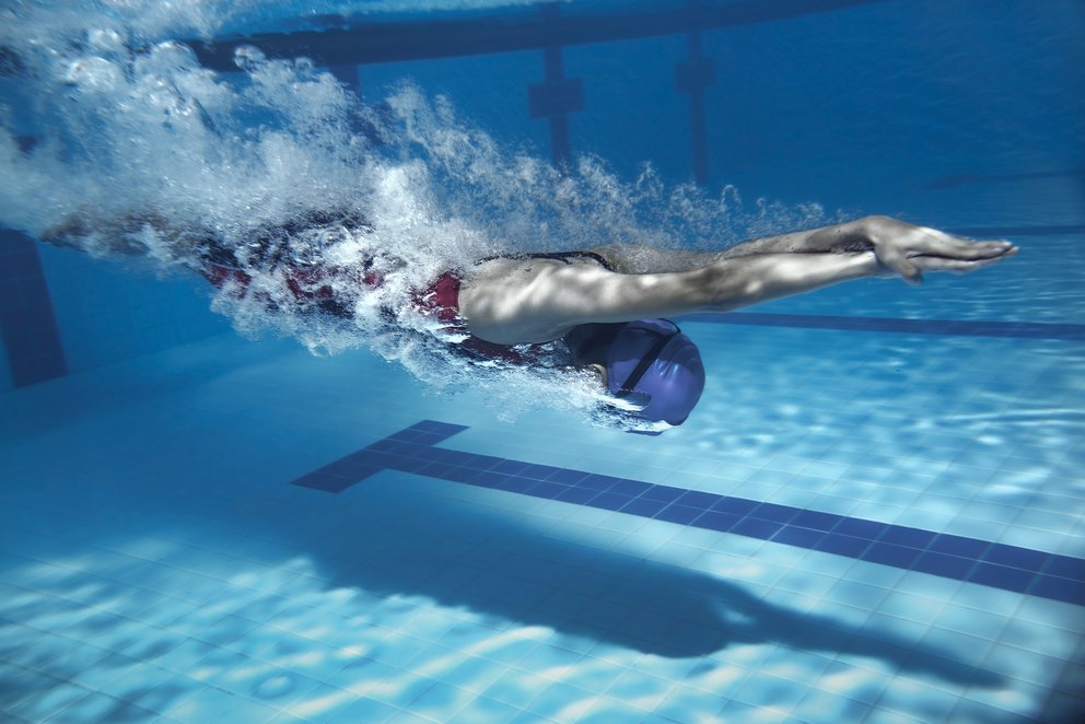 Ein Schwimmer im blauen Pool. Ein Schwimmer schwimmt in einem blauen Pool, während das Wasser sanft spritzt.