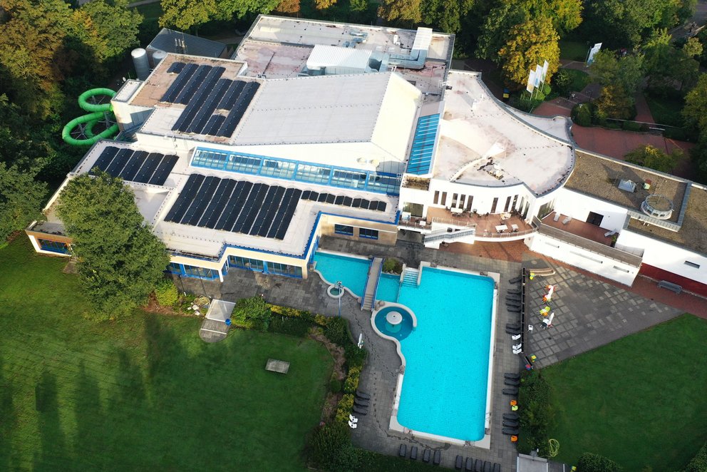 Luftaufnahme eines großen Schwimmbades. Luftaufnahme eines großen Schwimmbades mit einem Pool im Vordergrund, umgeben von grünen Bäumen und einem gepflegten Garten.