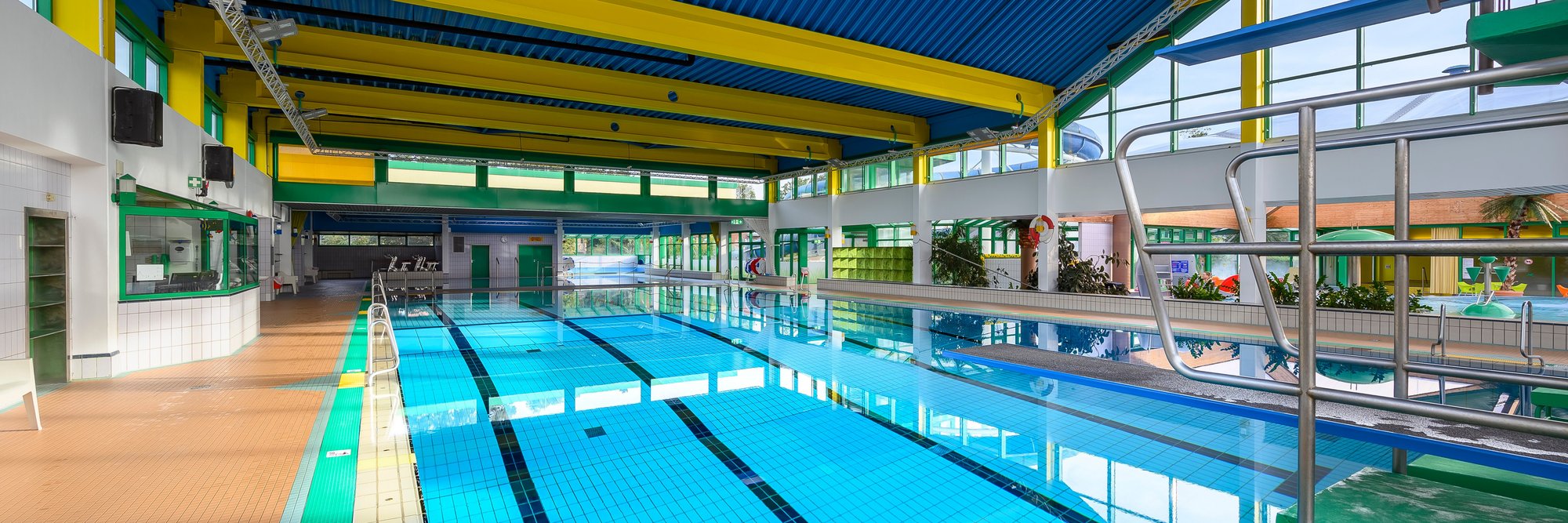 Großes Hallenbad mit blauer Decke, das Wasser spiegelt das Licht wider und schafft eine einladende Atmosphäre.