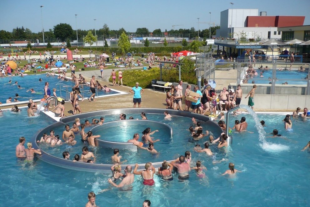 Freizeitpool mit schwimmenden Personen Ein weitläufiger Pool, gefüllt mit Menschen, die schwimmen und sich amüsieren, umgeben von Sonnenlicht und entspannter Atmosphäre.