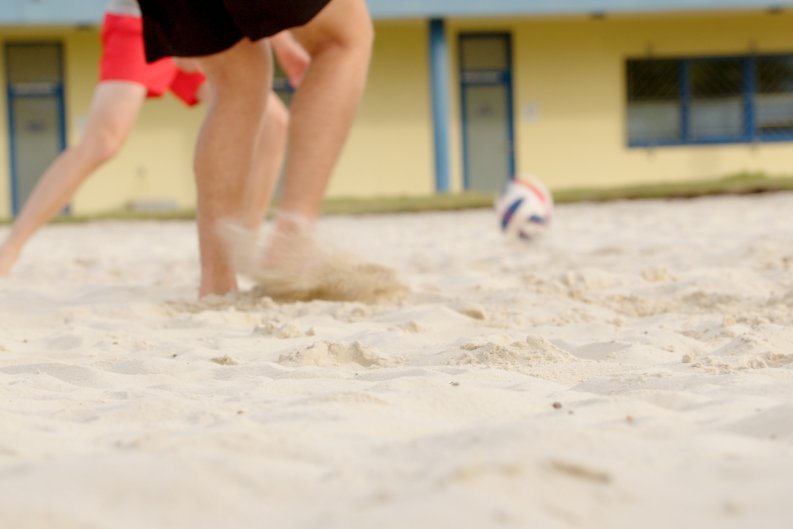 Beachvolleyball. Mehrere Personen spielen Beachvolleyball, während die Wellen im Hintergrund sanft an den Sand schlagen.