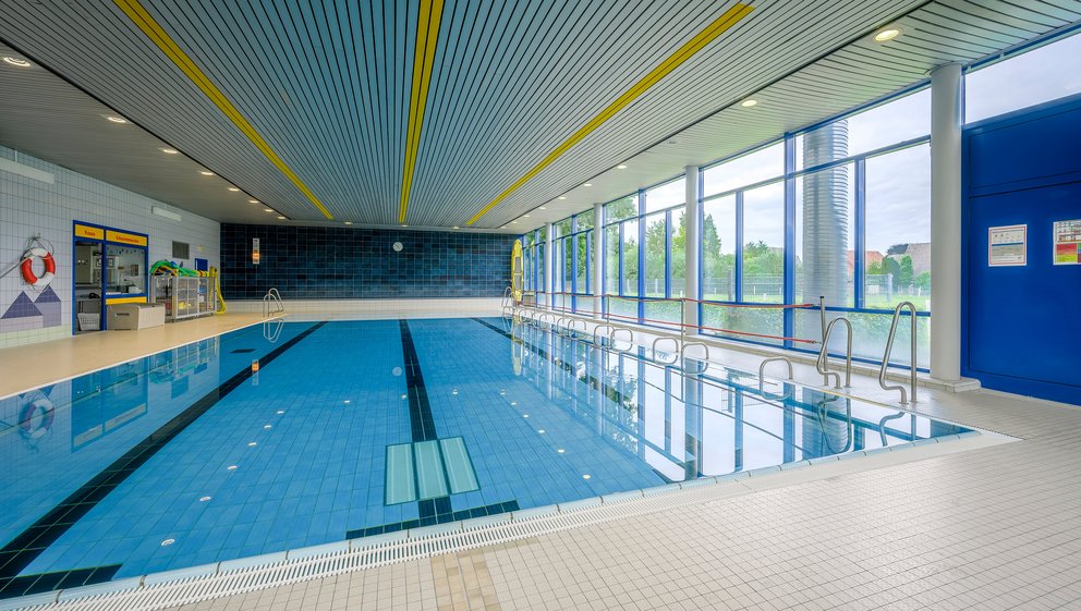 Großzügiger Indoor-Pool mit natürlichem Lichteinfall Ein Innenpool in einem großen Gebäude, umgeben von Fliesen und Fenstern, die natürliches Licht hereinlassen.