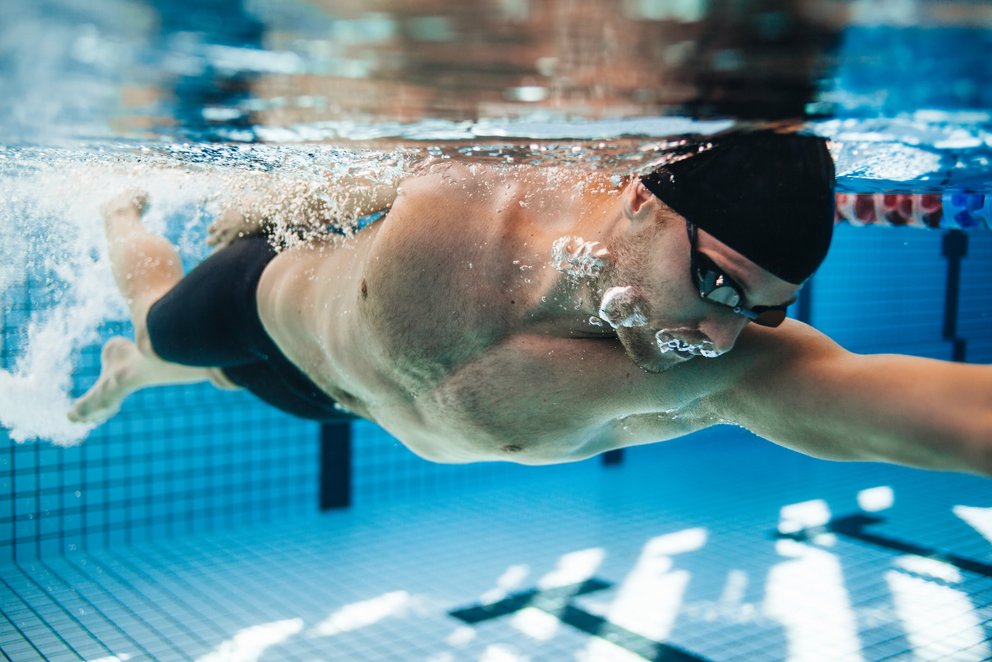Der Schwimmer im blauen Pool Ein Schwimmer schwimmt in einem blauen Pool, das Wasser spritzt um ihn herum.